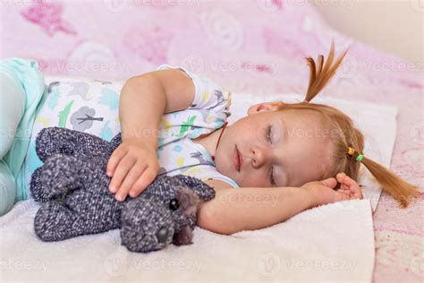 Una Niña Pequeña Está Durmiendo En Una Cama Con Juguetes Abrazados