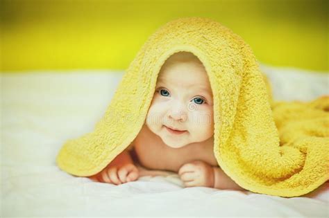 Happy Laughing Baby Wearing Yellow Hooded Towel Lies On Parents Bed