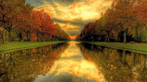 River Between Colorful Fall Autumn Trees Under Yellow Clouds Blue Sky