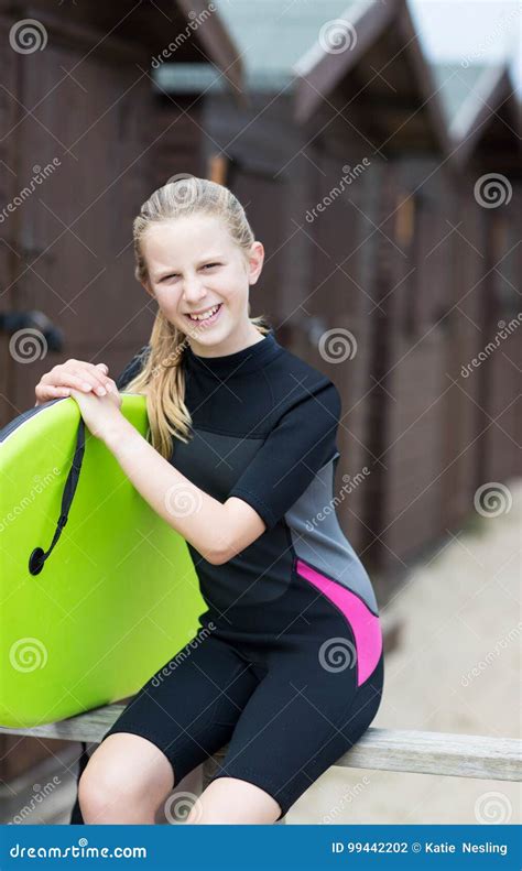 Portrait Of Girl By Beach Huts In Wetsuit Holding Bodyboard Stock Photo