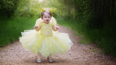 Cute Baby Girl Is Wearing Yellow Dress Standing On Road In Green Trees