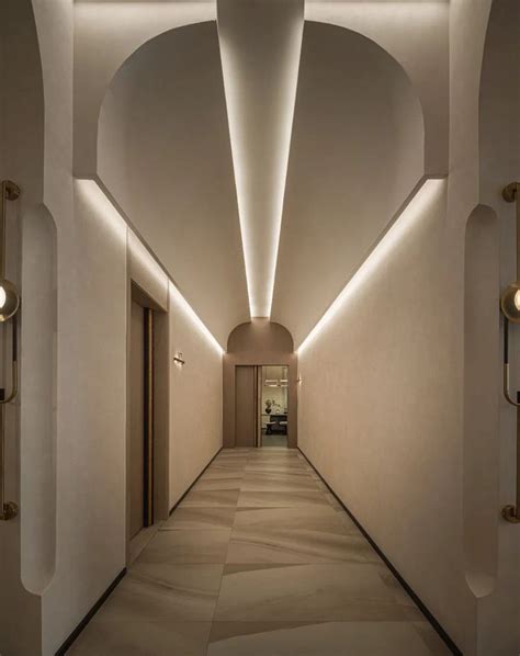 an empty hallway with white walls and lights on either side of the corridor leading to another room