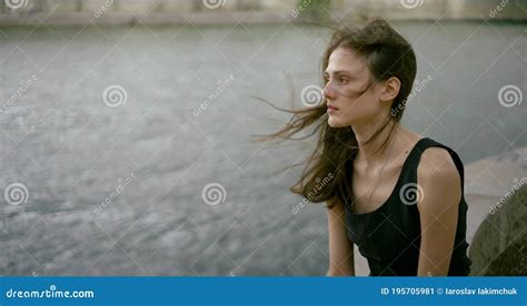 portrait of a slender dark haired girl model in a short black dress sitting on a tile near the