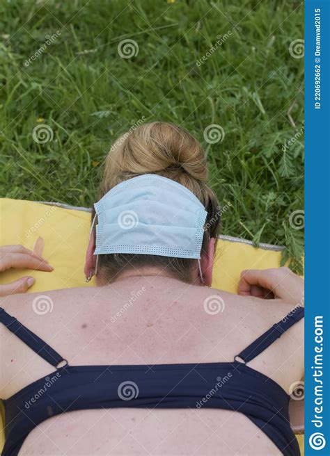 Woman Sunbathes Lying On A Rug In The Meadow She Has A Medical Mask On The Back Of Her Head
