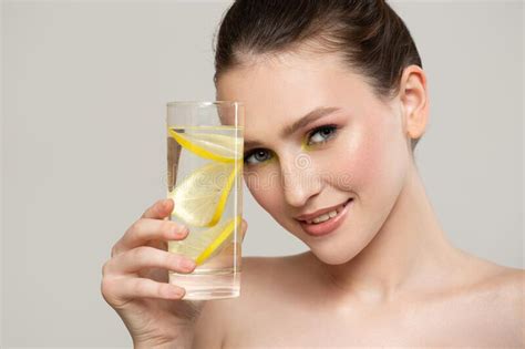 A Healthy Woman With Clean Skin Holds A Glass With Water And Lemon In
