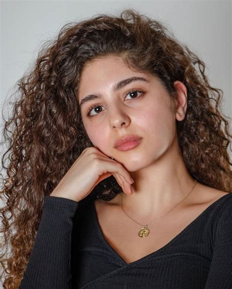 A Young Woman With Curly Hair Wearing A Black Shirt And Gold Necklace