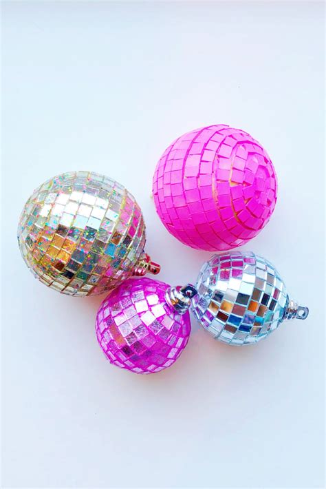 Three Shiny Disco Ball Ornaments On A White Surface With One Pink And