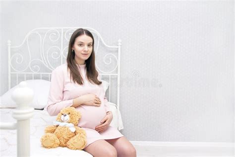 Pregnant Beautiful Girl Is Sitting On The Bed And Her Hands Are On Her