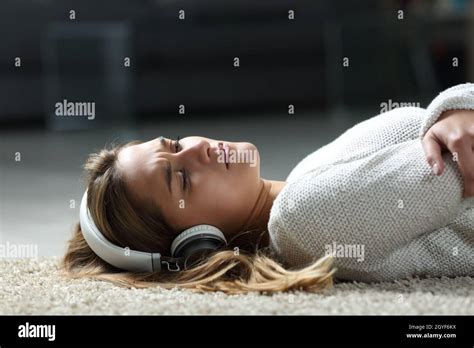 Sad Woman Listening To Music Wearing Headphones Lying On The Floor At