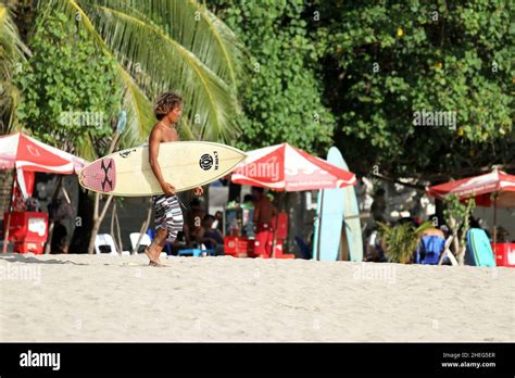 A Young Indonesian Man Walking Down The Beach And Carrying A Surboard