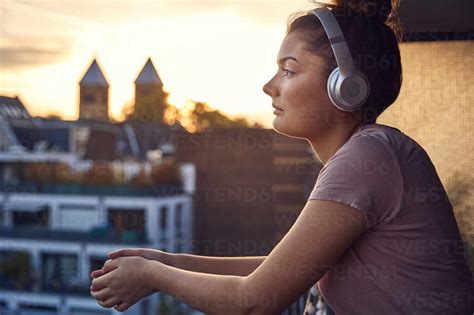 Young Woman Listening Music With Headphones On Balcony At Sunset Stock