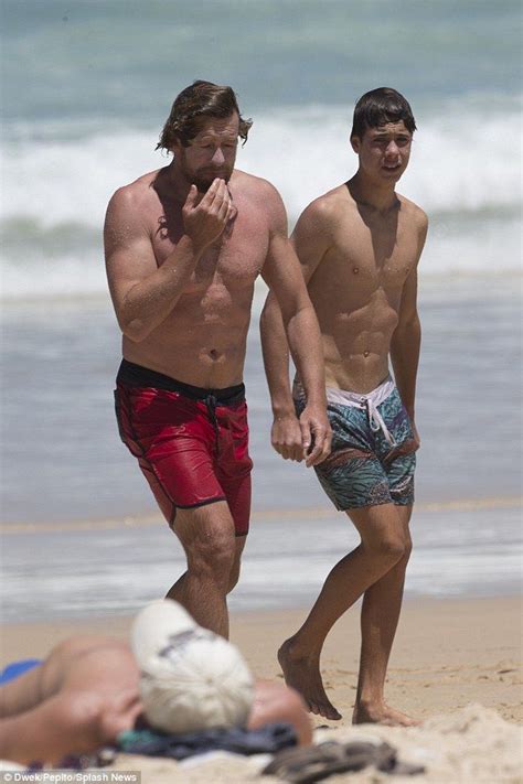 Two Men Walking On The Beach With One Holding His Hand To His Mouth And