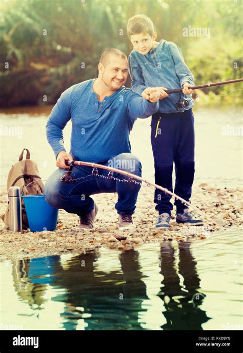 Portrait Of Glad Smiling Father And Cute Son Fishing With Rods In