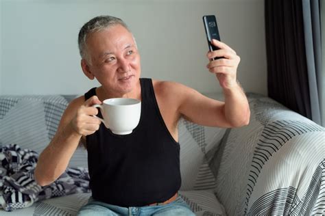 Premium Photo Happy Mature Japanese Man Drinking Coffee And Taking Selfie In The Living Room