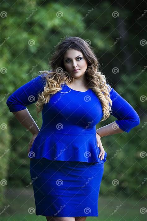 Young Beautiful Plus Size Model In Blue Dress Outdoors With Arms Akimbo