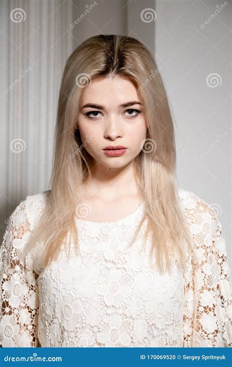 A Blonde Girl In A White Dress Poses In A White Photo Studio Stock