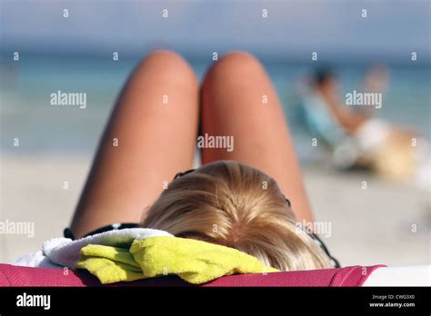 Vista Trasera De La Joven Mujer Rubia Tomando El Sol En La Playa De Arena Con El Mar De Fondo