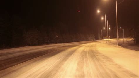 Car Driving At Night Through The Illuminated Part Of Snowy Freeway
