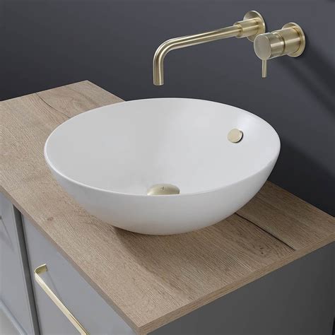 A White Bowl Sink Sitting On Top Of A Wooden Counter Next To A Faucet