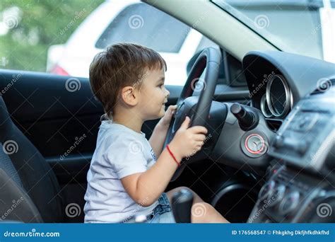 Little Boy Sits Behind The Wheel Of A Car And Dreams Of Driving A Car