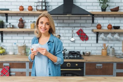 Free Photo Young Woman Holding Coffee Mug In Hand Standing In The Kitchen