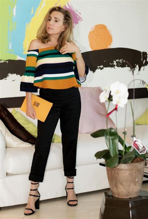 A Woman Standing In Front Of A Couch Wearing Black Pants And Striped Shirt With Yellow Clutch Bag