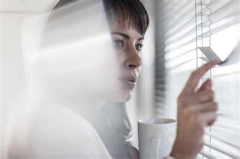 Woman In Office Looking Through Blinds Stock Photo