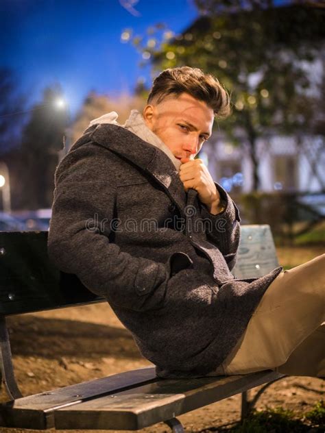 Handsome Trendy Young Man Sitting On Bench At Night Stock Photo