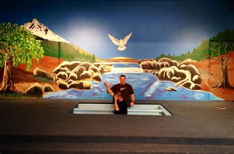 A Man Sitting On A Bench In Front Of A Mural With Mountains And Trees