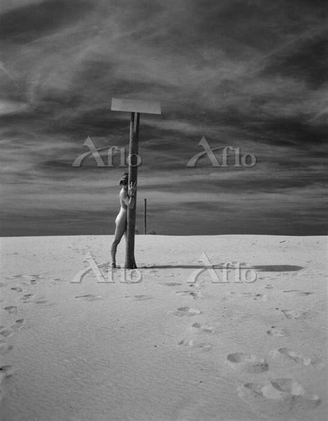 Nude woman standing behind pole on beach b w の写真素材 アフロ
