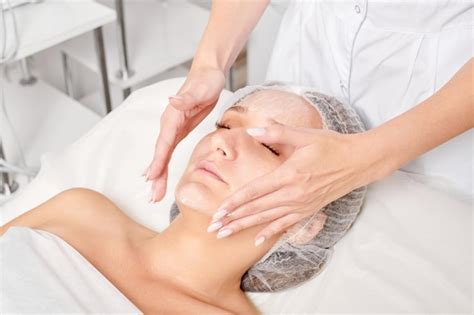 Premium Photo Cosmetologist Rubbing Moisturizing Cream Mask Into Woman Face Skin For