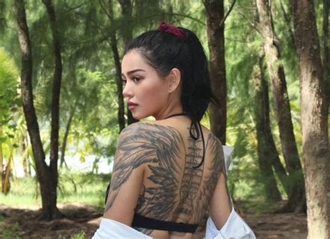 A Woman With Tattoos On Her Back Standing In The Woods