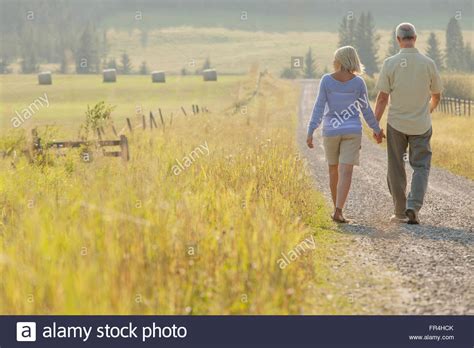 View From Behind Of Middle Aged Couple Walking Down Country Road Stock