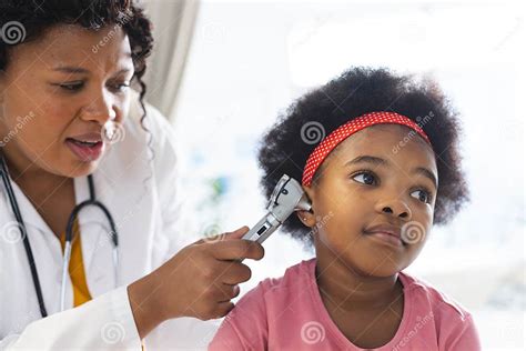 African American Female Doctor Examining Girl Patient Using Otoscopy At