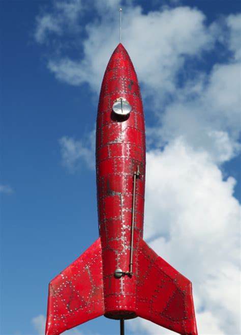 A Large Red Rocket Shaped Object On Top Of A Metal Pole In Front Of A