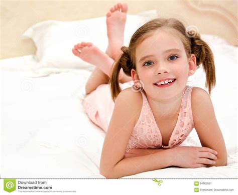 Прелестная усмехаясь маленькая девочка отдыхает на кровати Стоковое Изображение изображение
