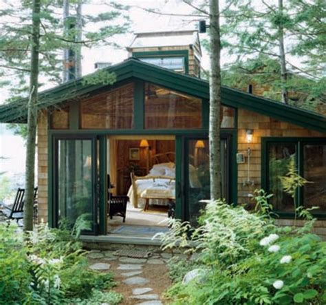 A Small Cabin In The Woods Surrounded By Greenery And Trees With A Bed