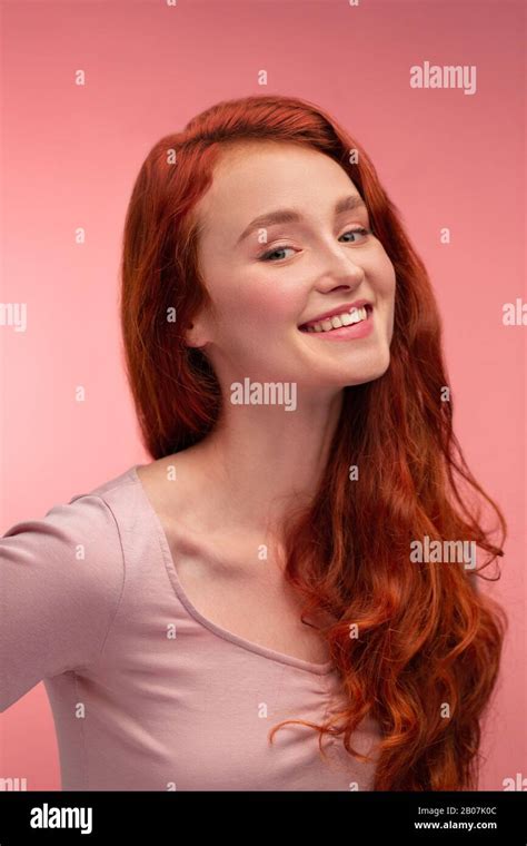 portrait of smiling redhead girl perfect skin beautiful female model with long hair over pink