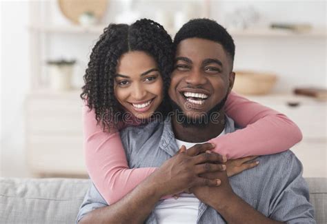 Loving African American Couple Hugging At Home And Looking At Camera