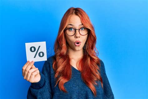 Young Beautiful Redhead Woman Holding Percentage Symbol Scared And Amazed With Open Mouth For