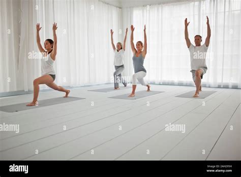 Group Of People Lunging With Arms Overhead At A Yoga Class Stock Photo