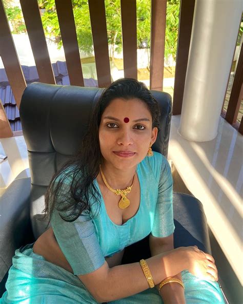 A Woman Sitting In A Chair Wearing A Blue Sari And Gold Jewelry On Her Neck