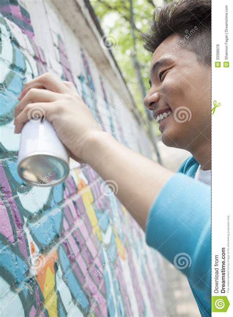 Усмехаясь молодой человек держа картину баллончика и брызга на стене снаружи Стоковое Фото