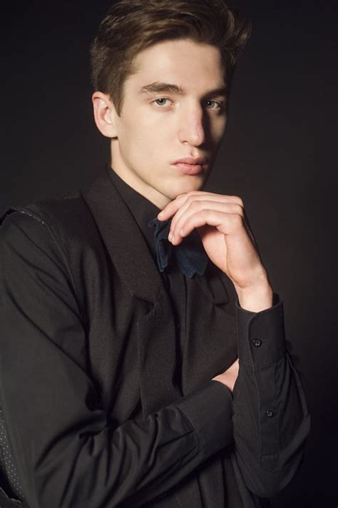 A Young Man In A Black Suit Posing For The Camera With His Hand On His Chin