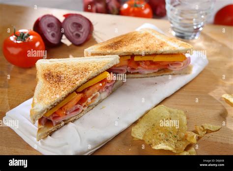 Toasted Ham Cheese Tomato Sandwich On A White Napkin On A Wooden Breadboard With Whole Tomatoes