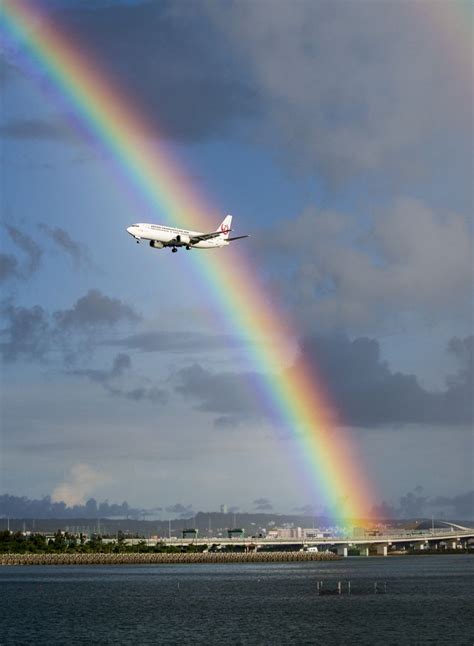 An Airplane Is Flying Over The Water With A Rainbow In The Sky Above It