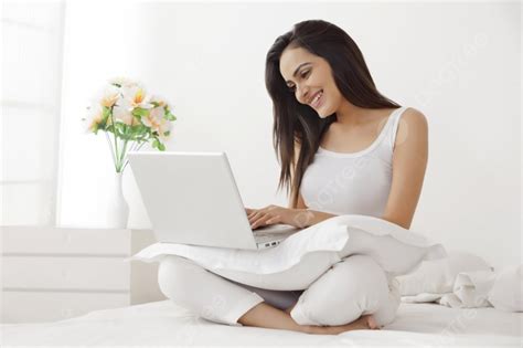 امرأة شابة جميلة في ملابس نوم تستخدم كمبيوتر محمول على السرير صورة الخلفية والصورة للتنزيل