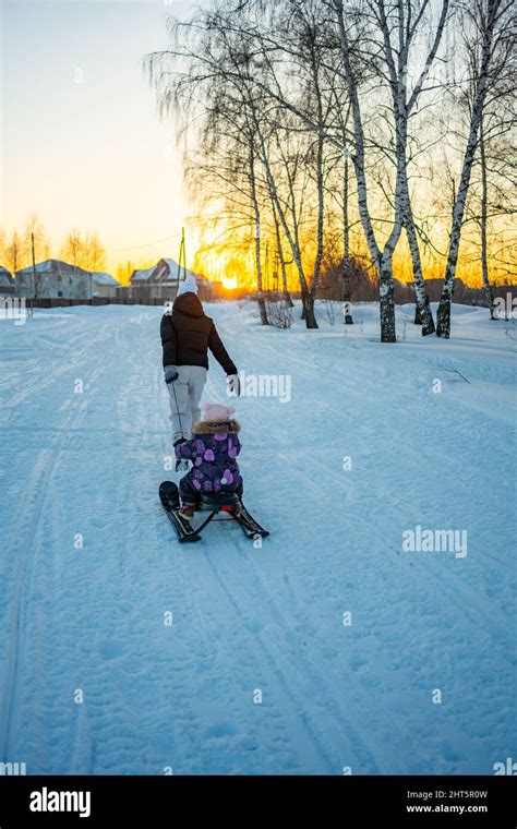 Young Woman Pulling Plastic Sled With Little Child Across Snowy