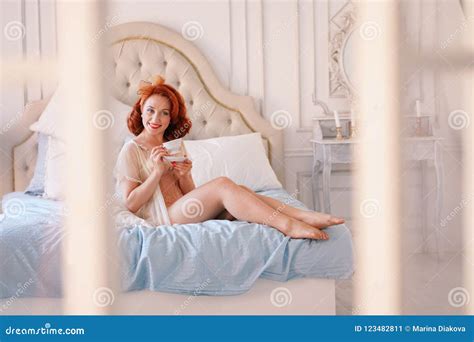 A Luxurious Pin Up Lady Dressed In A Beige Vintage Lingerie Posing In Her Bedroom And Have A Cup