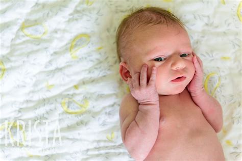 Naked Newborn Baby Girl With Hands On Cheeks In Yellow White And Gray Nursery During Lifestyle